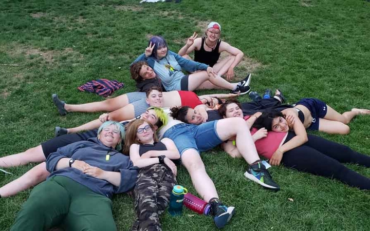 a group of students lay in a pile on grass during an outward bound trip for lgbtq+ teens